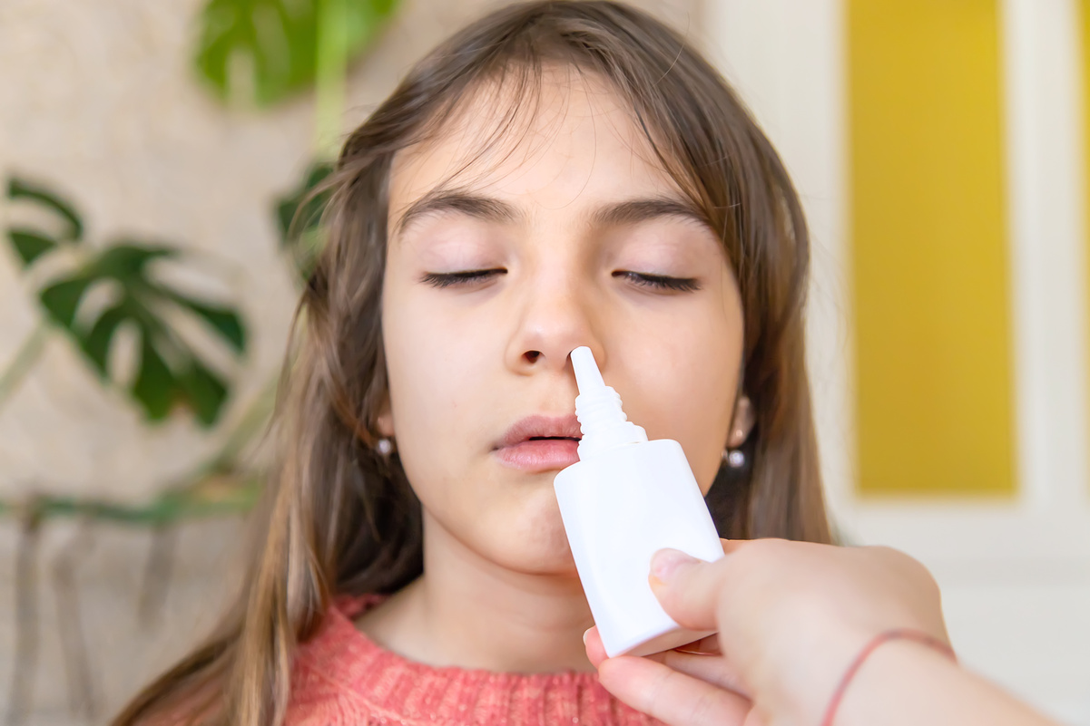 Mother Giving Nasal Spray Inhaler To Daughter At Home